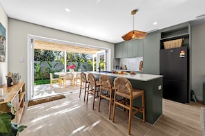 A modern kitchen with a central island, bar stools, a dining area with a table and chairs, and a view of the garden.