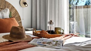 En pænt redt seng med et magasin, en hat og en bakke med kaffekande og kop.