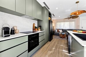 A modern kitchen with a built-in oven, a coffee machine, and a dining area with a sofa and a table.