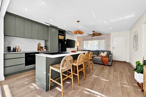 Una cocina moderna con una isla central, electrodomésticos integrados y un comedor con sillas de mimbre.