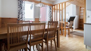 A dining area with wooden chairs and a table, a kitchen area with a refrigerator, and a staircase leading to an upper level. - Åre Fjällby (Are)