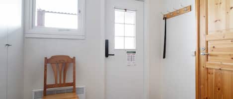 Une pièce avec une chaise en bois, une porte dotée d’une fenêtre et un porte-manteau.