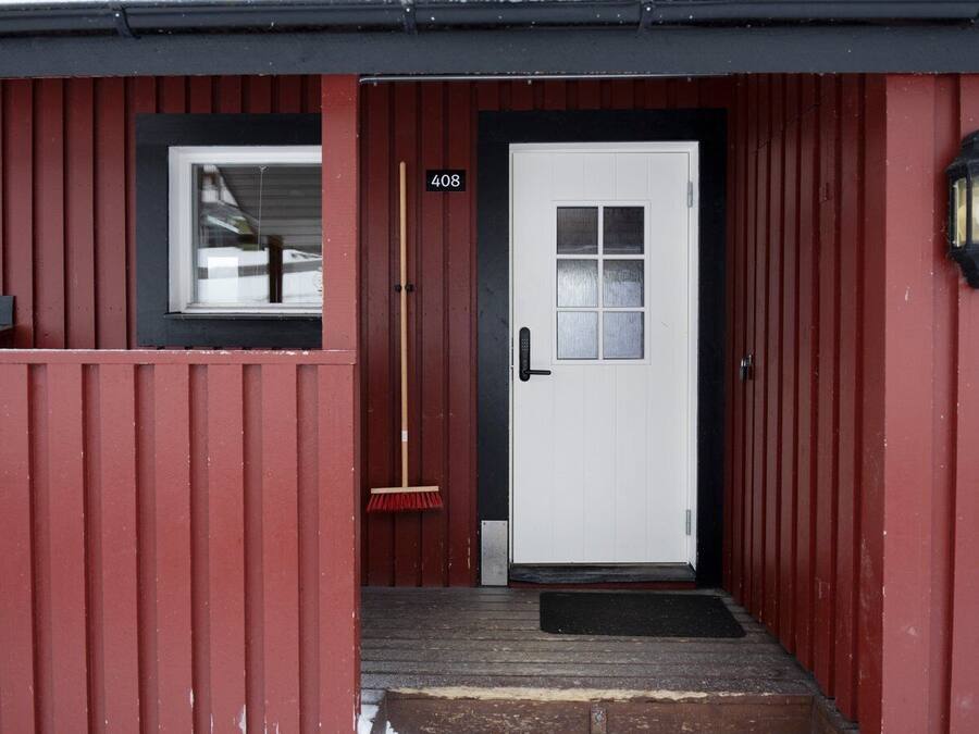 A red building with a white door, a number '408' sign, a window, and a broom leaning against the door.