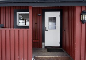 A red building with a white door, a number '408' sign, a window, and a broom leaning against the door. - Åre Fjällby (Are)
