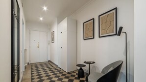 Ein Korridor mit Schachbrettboden, einem Sessel, einem kleinen Tisch und gerahmten Kunstwerken an der Wand.