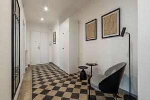 Ein Korridor mit Schachbrettboden, einem Sessel, einem kleinen Tisch und gerahmten Kunstwerken an der Wand.