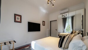 Ein Schlafzimmer mit einem Bett, einem an der Wand befestigten Fernseher, einem Spiegel und einer Tür zu einem Badezimmer.