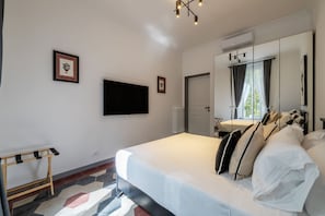 Ein Schlafzimmer mit einem Bett, einem an der Wand befestigten Fernseher, einem Spiegel und einer Tür zu einem Badezimmer.