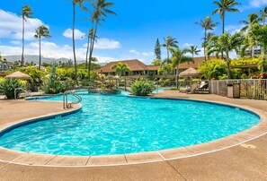 Ein Pool mit gewölbter Kante, umgeben von Palmen und Liegestühlen.