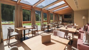 Un comedor moderno con luz natural, mesas, sillas y vistas a un paisaje montañoso.