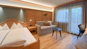 Habitación de hotel con una cama de madera, un sofá, una mesita y una ventana con cortinas.