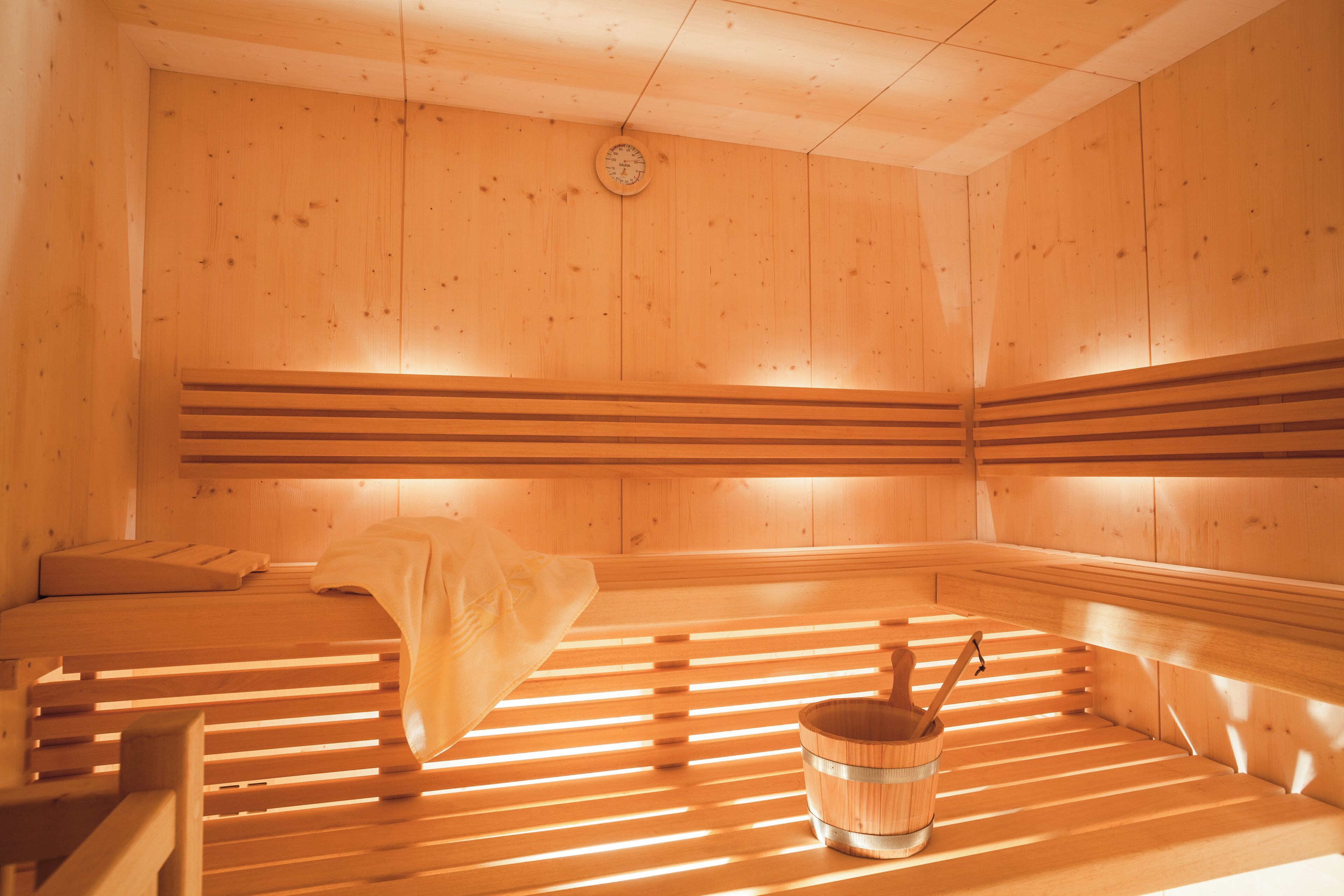 Una sauna con bancos de madera, un banco con una toalla y un balde de madera.