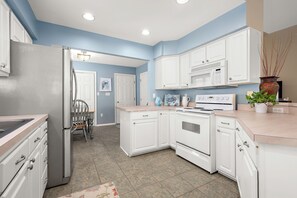 A kitchen with white cabinets, a refrigerator, a microwave, and a stove. There is a chair and a door leading to another room. - Pond Front Home with Magnificent Sunset views from the gorgeous Screened porch! (Lewes)