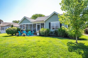 A two-story house with a covered porch, a lawn, and a tree. - Pond Front Home with Magnificent Sunset views from the gorgeous Screened porch! (Lewes)
