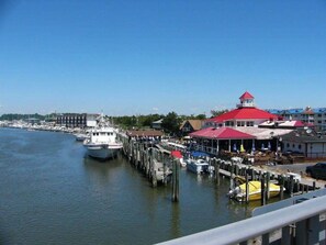 A waterfront marina with boats docked, a red-roofed building, and a clear blue sky. - Pond Front Home with Magnificent Sunset views from the gorgeous Screened porch! (Lewes)