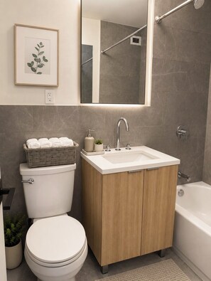Et badeværelse med toilet, håndvask med spejl over, badekar og en plant i ramme på væggen.