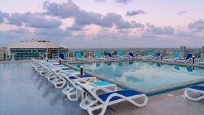 A rooftop pool with lounge chairs and a cityscape view. - Naya Suites; Luxury 2BR Panoramic Sea & Lagoon View, Beach Towers (Marsa Matrouh)