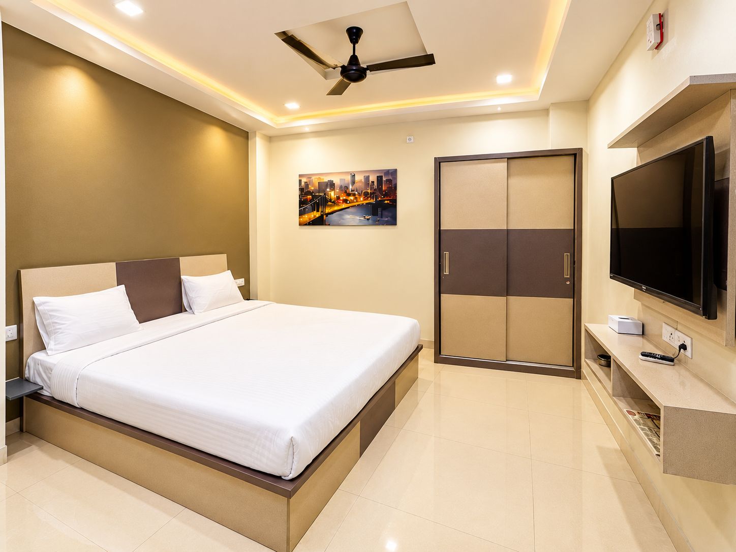A hotel room with a bed, a television, a wardrobe, and a painting on the wall.