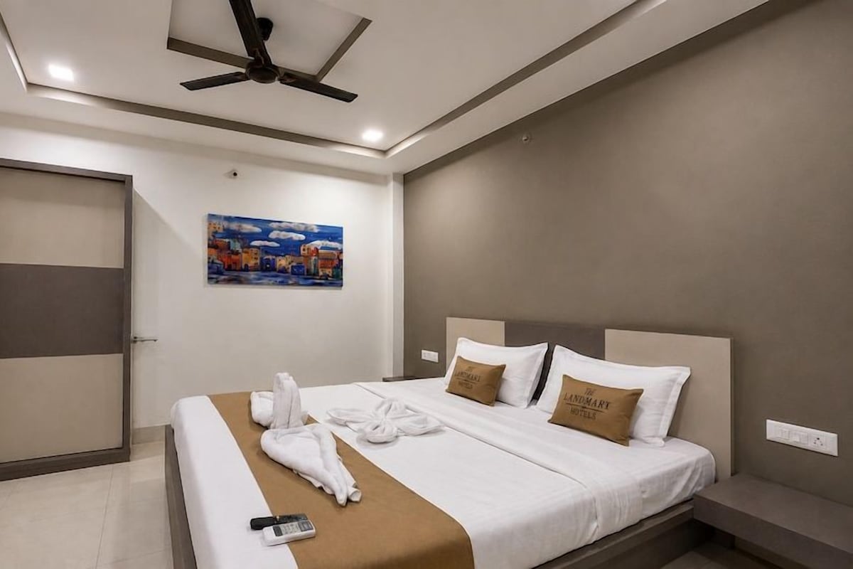 A hotel room with a bed, a ceiling fan, a painting, and a brown throw blanket.