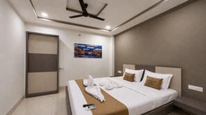 Une chambre d’hôtel avec un lit, un ventilateur de plafond, un tableau et un plaid marron.