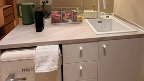 A kitchenette with a stainless steel range hood, a sink, a coffee maker, and a storage unit with hanging utensils. - Bluewaves Antiparos Sunstone Terrace House (ANTIPAROS)