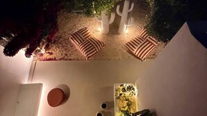 A nighttime outdoor seating area with a cactus sculpture, a small table, and a wall-mounted planter with flowers. - Bluewaves Antiparos Sunstone Terrace House (ANTIPAROS)