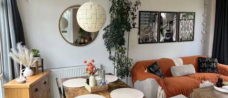 A modern living room with a wooden dining table, a sofa, and a large mirror.