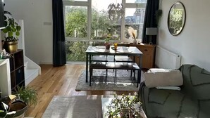 Een woonkamer met een eettafel, een bank en uitzicht op groen.