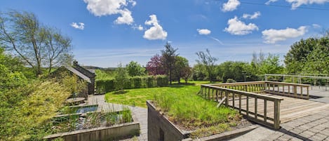 A garden area with a wooden deck, stone walls, and a small pond.