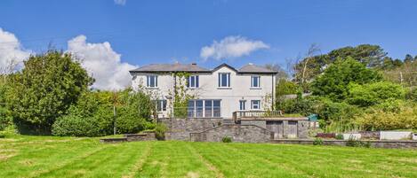 A two-story house with a stone wall and a grassy lawn in front.