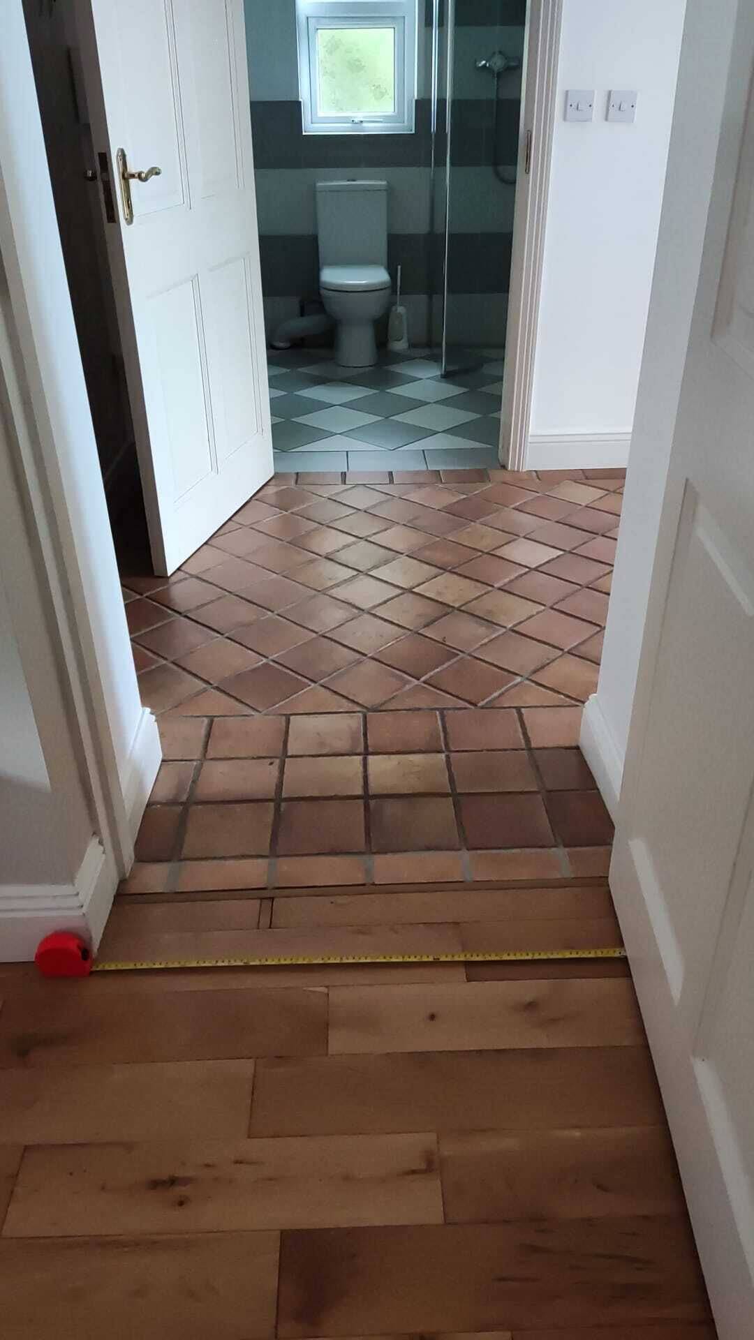 A hallway with a tiled floor leading to a bathroom with a toilet and a shower.