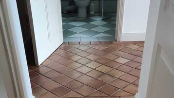 A hallway with a tiled floor leading to a bathroom with a toilet and a shower.