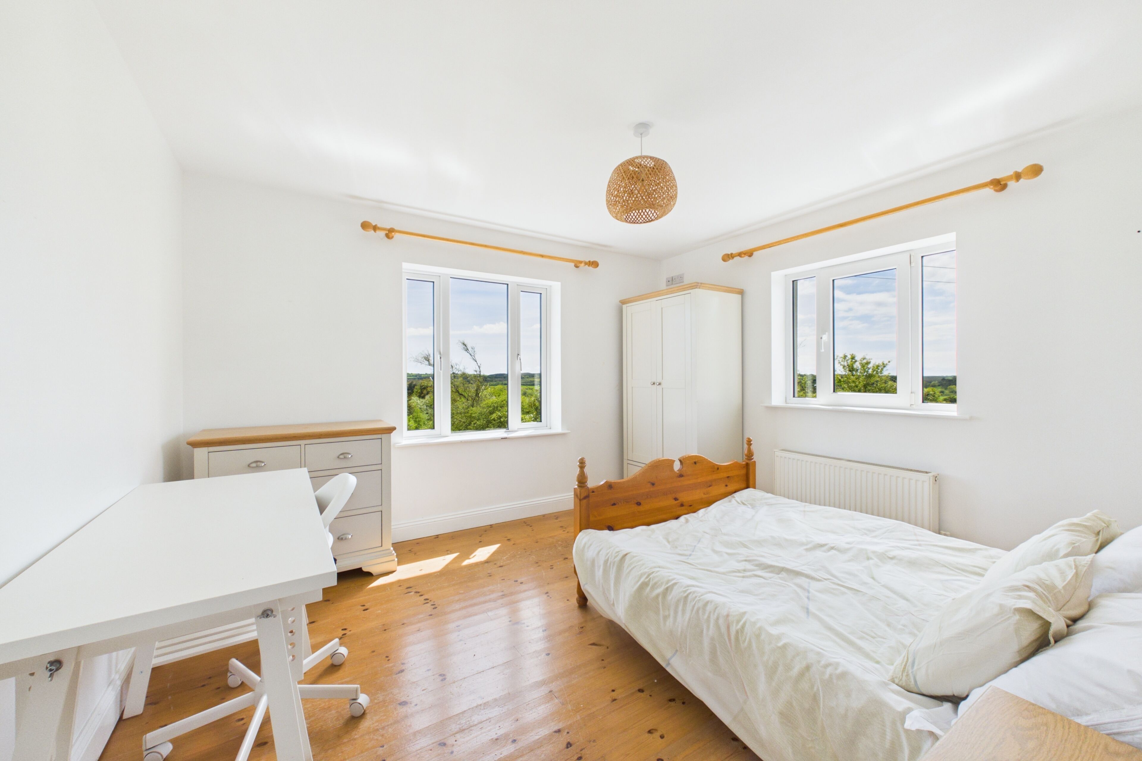A bedroom with a bed, a desk, and two windows.