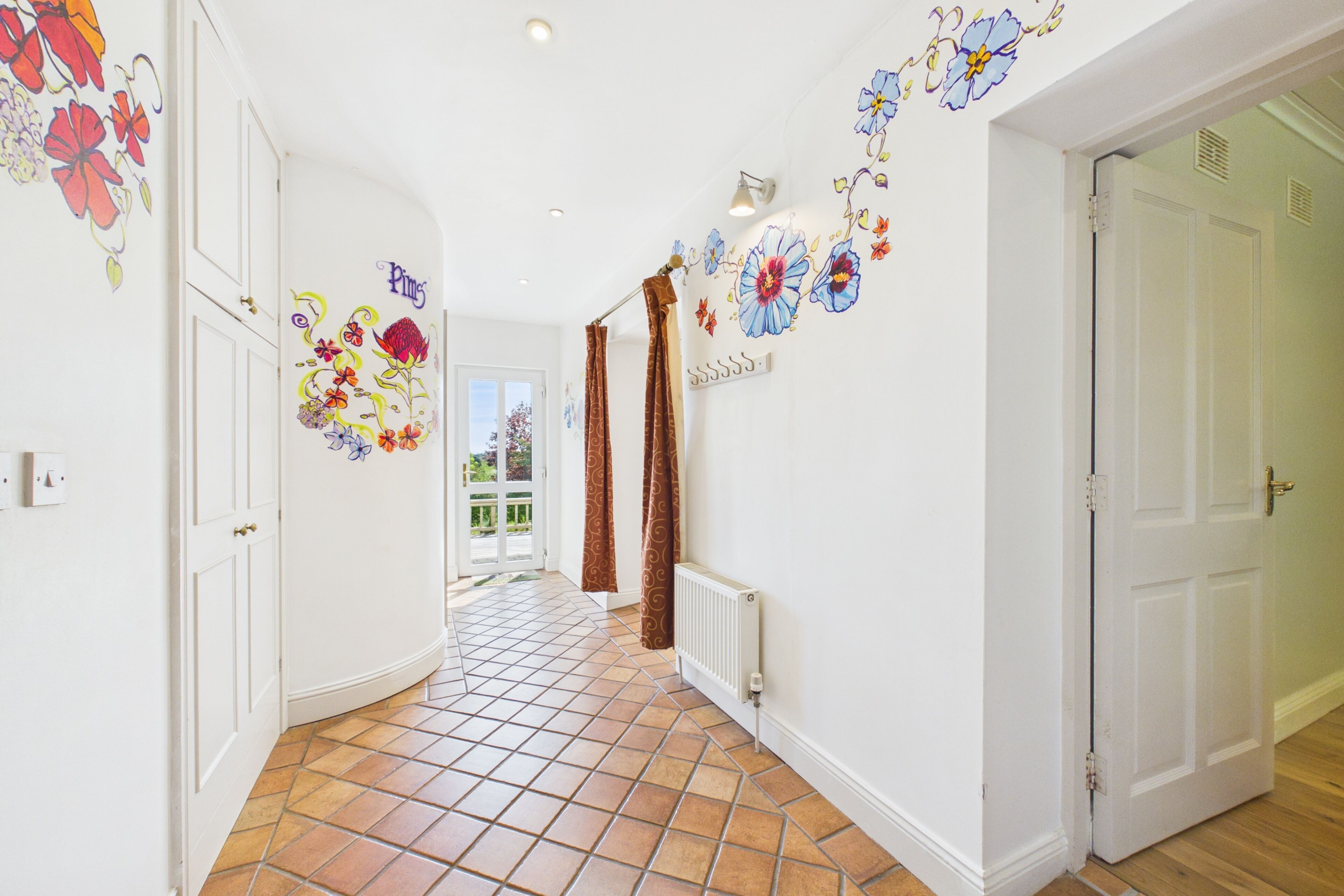 A hallway with tiled flooring, white walls, and floral wall art.