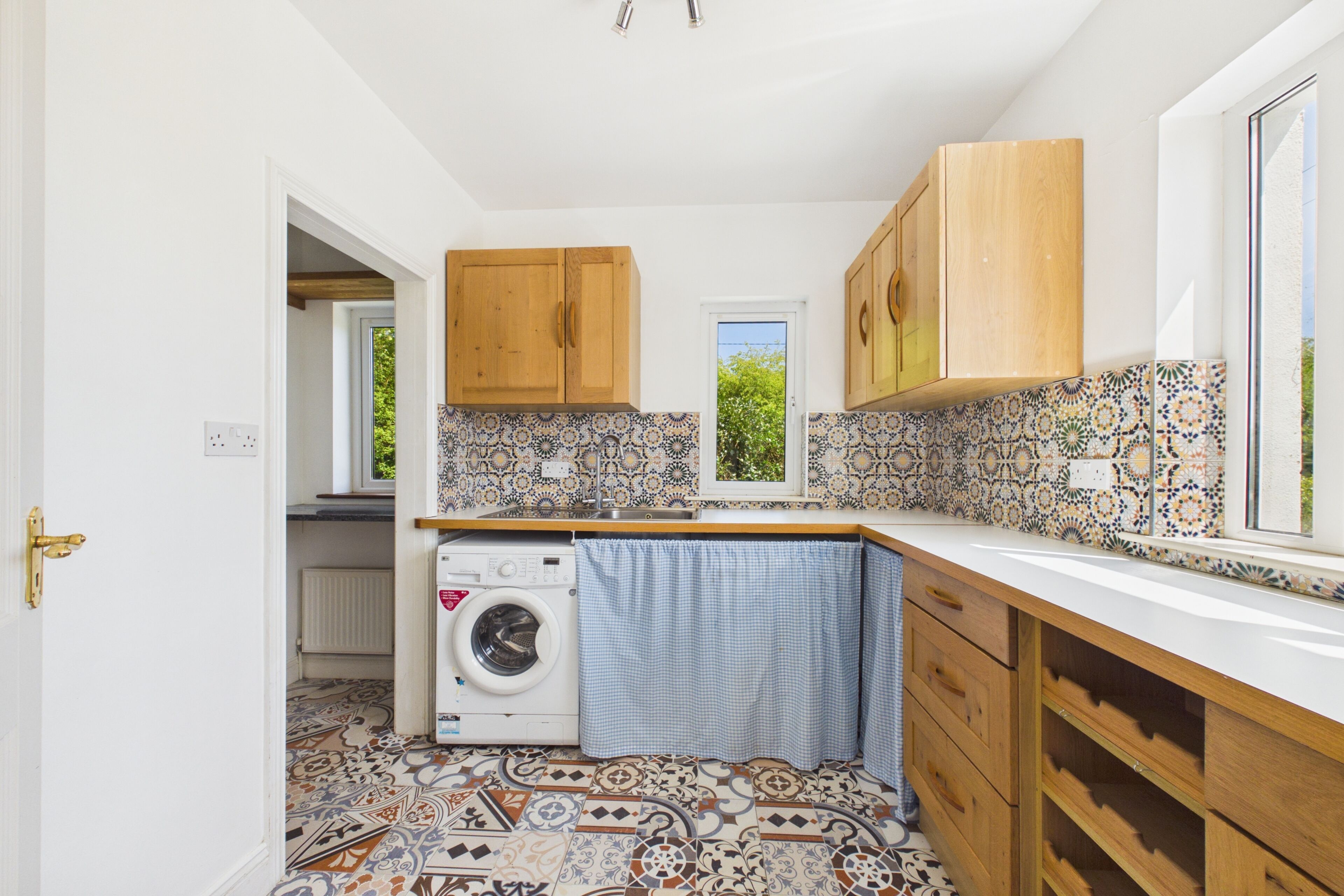 Une cuisine de taille réduite, dotée de meubles en bois, d’un lave-linge et d’un revêtement de sol carrelé à motifs.