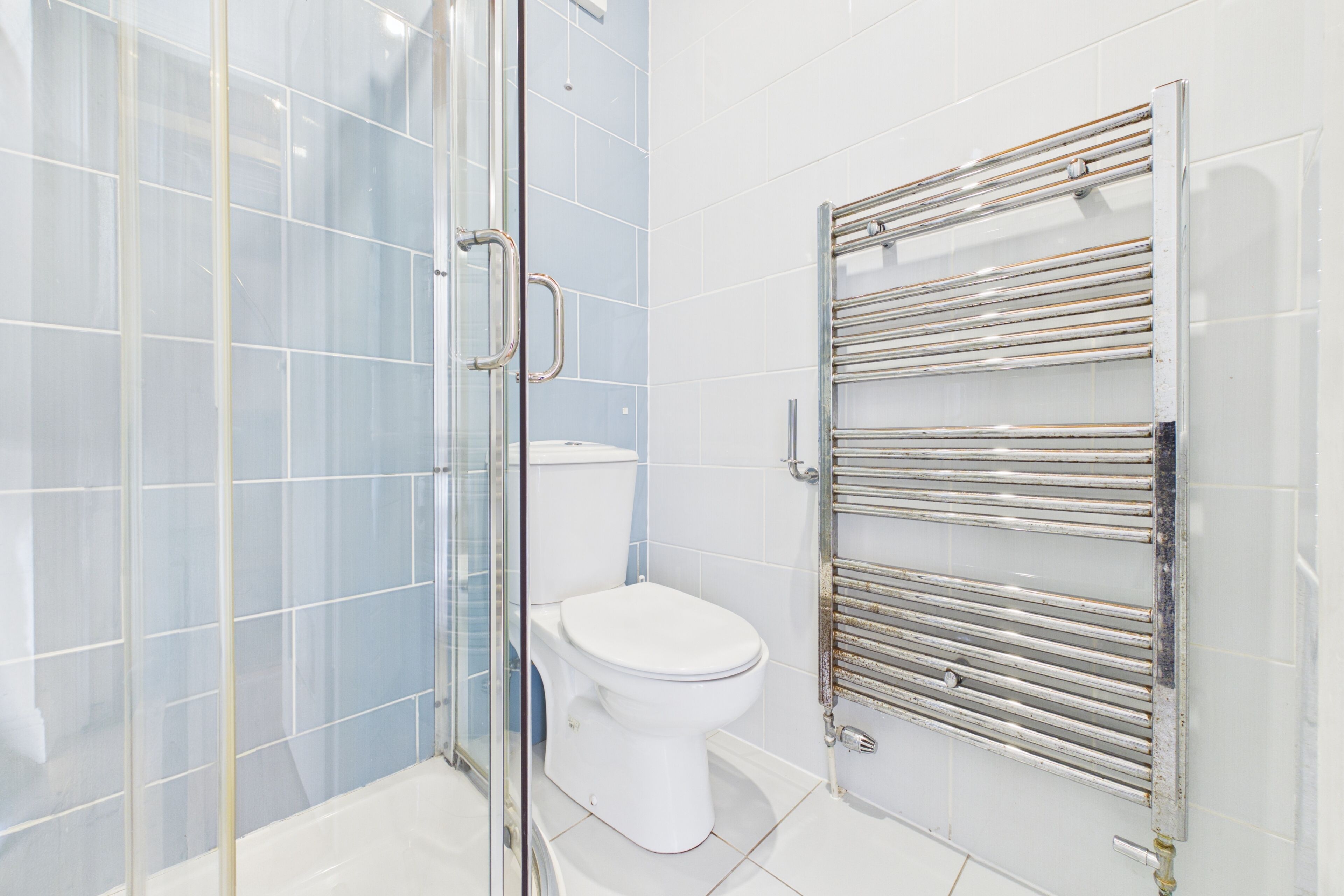 A modern bathroom with a glass shower enclosure, a white toilet, and a chrome towel rack.