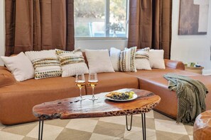 A living room with a brown sofa, patterned cushions, a wooden coffee table with two glasses of wine, and a plate of fruit. - 49 North Oasis • Heated Pool • Spa • Mini-Golf • Game Room (Scottsdale)