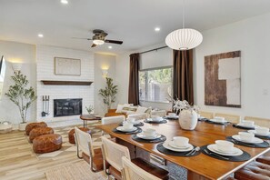 A modern dining room with a large wooden table set for a meal, a fireplace, and a ceiling fan. - 49 North Oasis • Heated Pool • Spa • Mini-Golf • Game Room (Scottsdale)