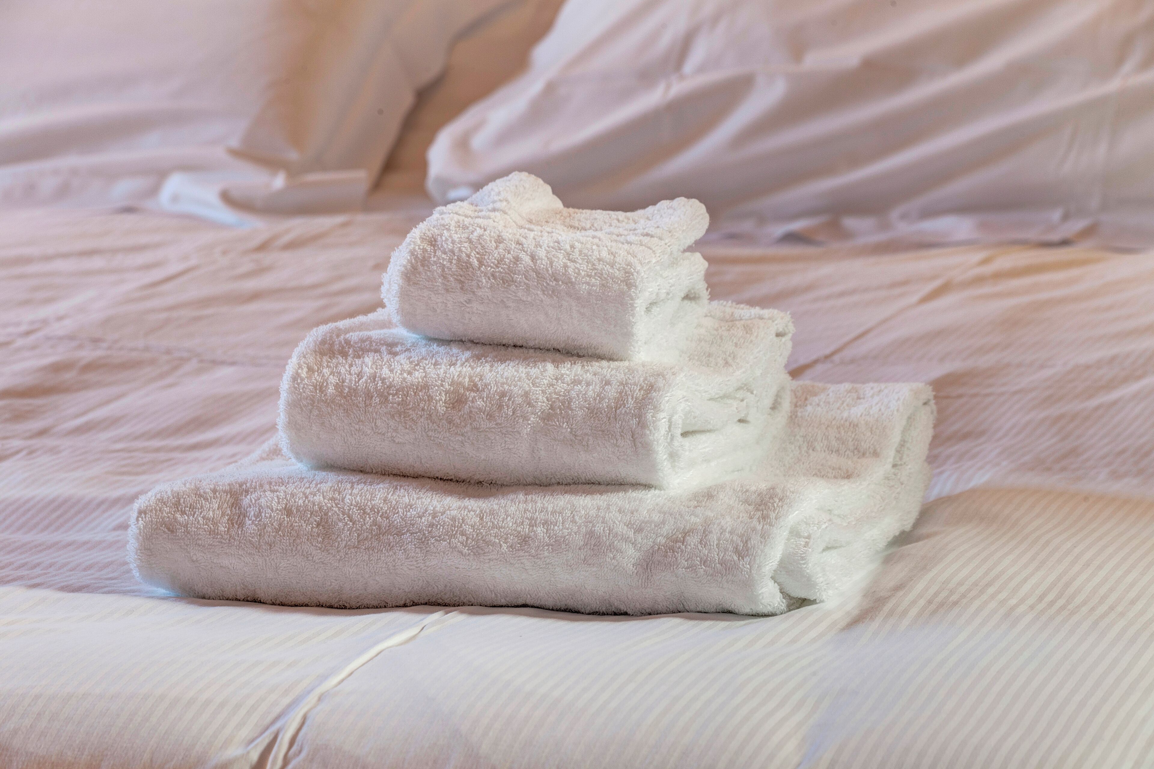 A bed with neatly folded white towels stacked in a pyramid shape.