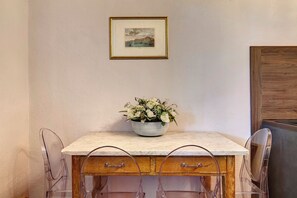 Un coin repas avec une table en marbre, des chaises transparentes, un buffet en bois et un tableau encadré au mur.