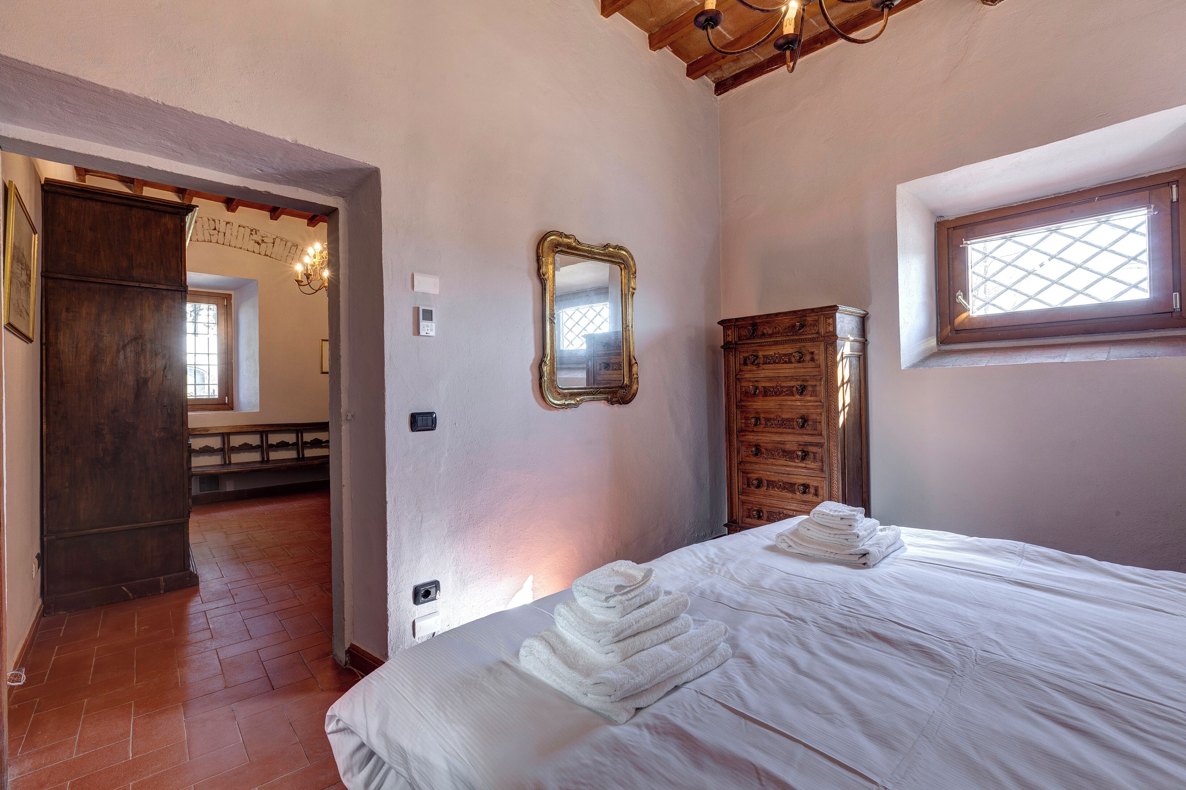 Een slaapkamer met een bed, een houten garderobe, een spiegel en een raam.