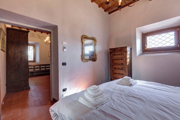 A bedroom with a bed, a wooden wardrobe, a mirror, and a window.