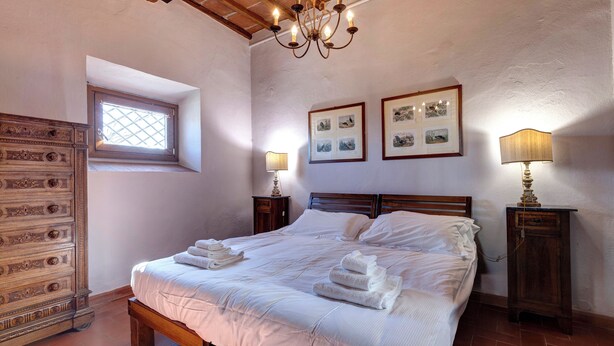 Un dormitorio con una cama de madera, dos mesitas de noche con lámparas, una ventana con vistas y una pared decorada con marcos.