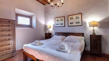 A bedroom with a wooden bed, two bedside tables with lamps, a window with a view, and a wall with framed pictures.
