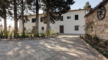 A building with a gravel driveway, a stone wall, and a row of trees.