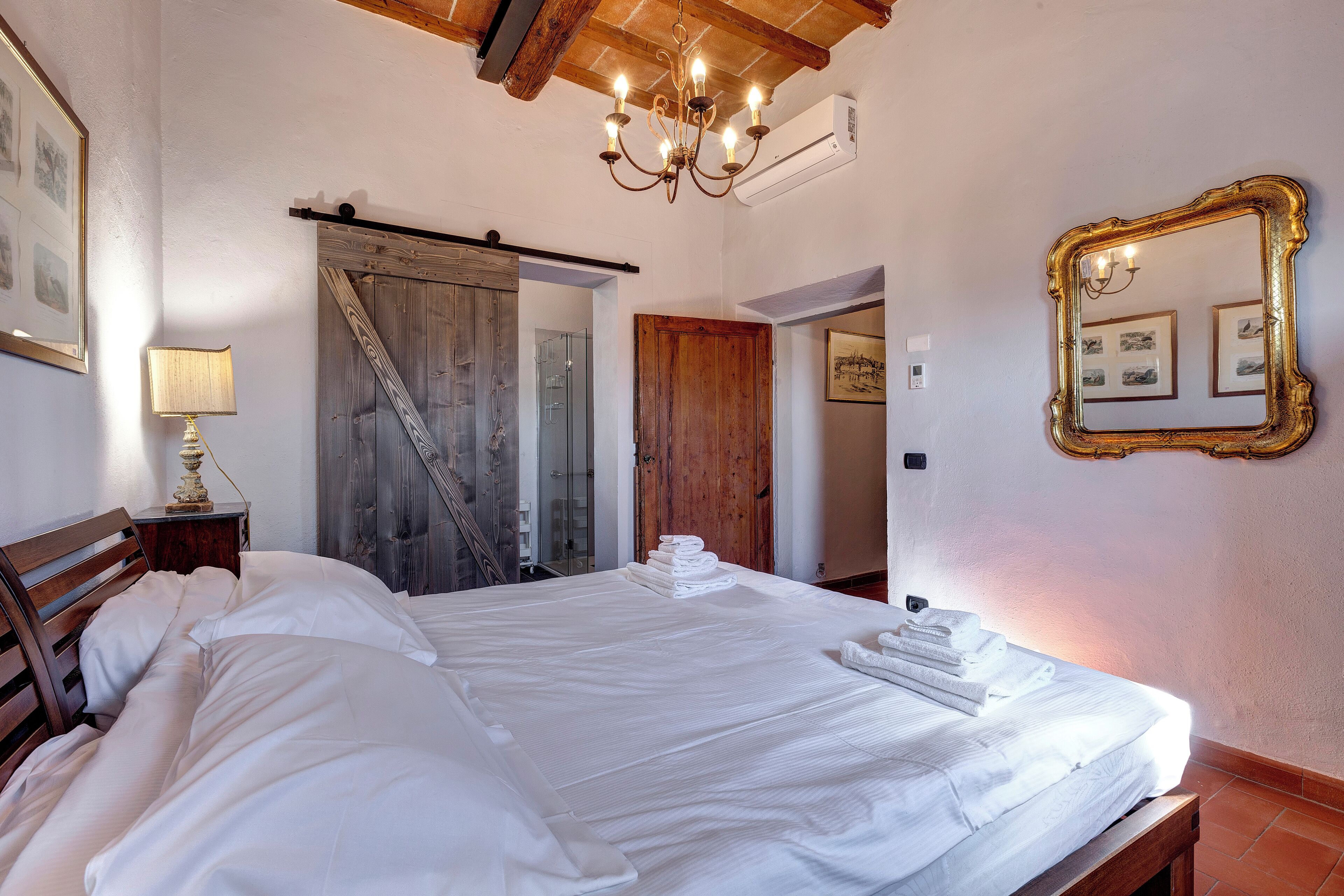 Habitación de hotel con una cama grande, techo de madera, candelabro y un espejo en la pared.