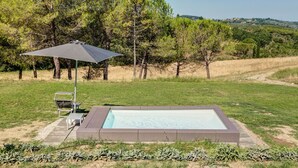 Piscina rectangular al aire libre con un borde oscuro, rodeada por un césped con árboles y cielo despejado.