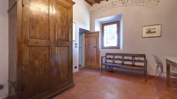 A room with a large wooden wardrobe, a bench, a window with a view, and a wall-mounted picture.
