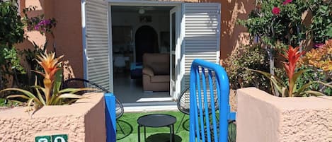 A hotel entrance with a sliding door, a small patio area with a table and chairs, and a number sign indicating the location.