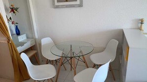 Et spiseområde med et glasbord omgivet af hvide stole, et hvidt skab og en blå vase på en hvid bordplade.